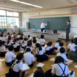 学校訪問写真（教室で当事者の話を聞いている小学生たちの後ろ姿。）